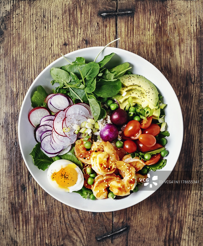 健康的午餐碗，有绿色蔬菜，鳄梨，圣女果，萝卜，水煮鸡蛋，和虾在木制的背景图片素材