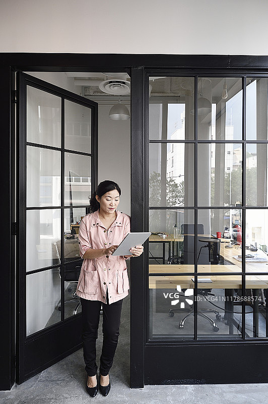 一名中国妇女在一间玻璃办公室里使用平板电脑图片素材