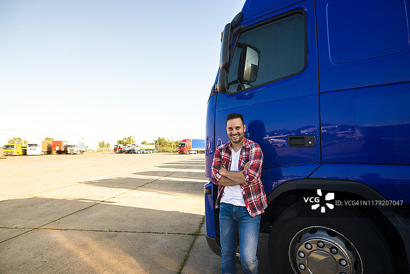 微笑的卡车司机站在他的卡车准备驾驶的肖像。司机的职业。运输服务。图片素材