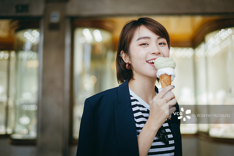 快乐的年轻亚洲女性游客一边享受冰淇淋，一边探索和走过意大利当地的城市街道图片素材