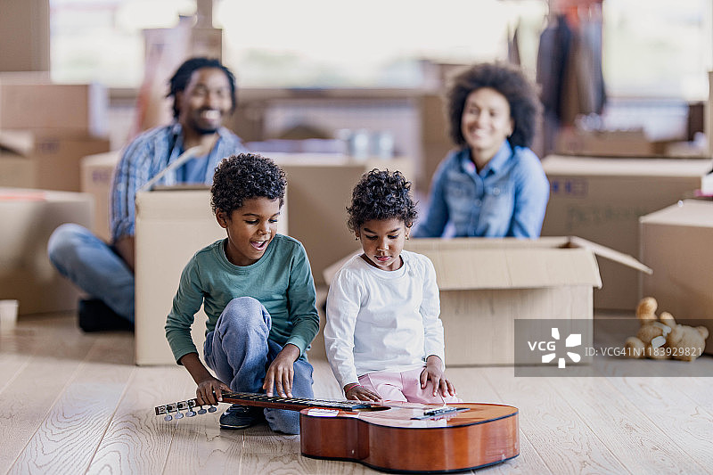 快乐的非裔美国兄弟和姐妹玩吉他在他们的新家。图片素材