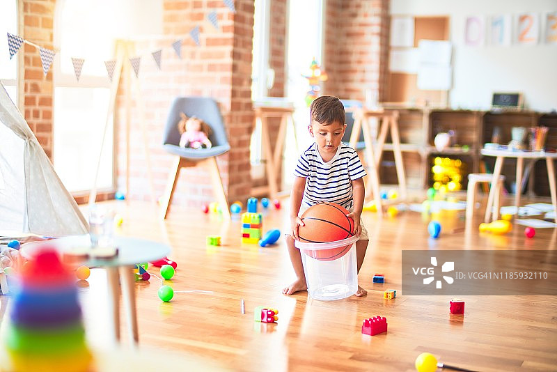 漂亮的学步男孩在幼儿园玩篮球和塑料篮子图片素材