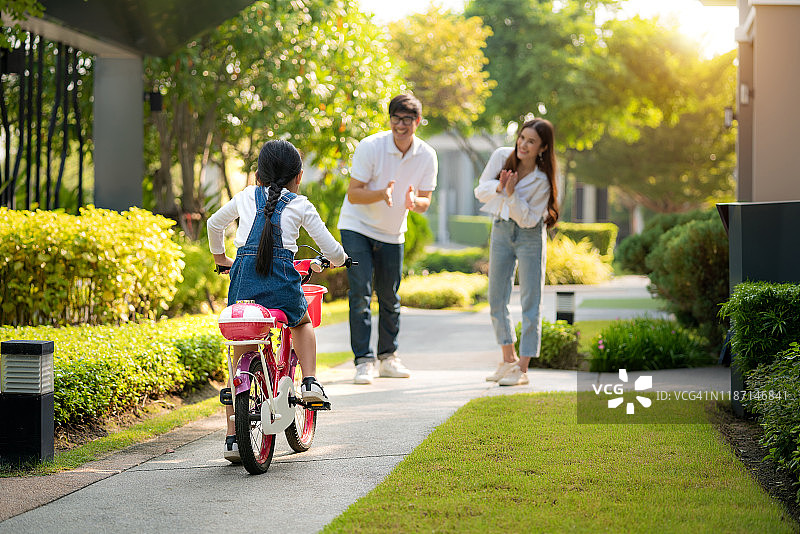 快乐的亚洲父母和父母教他们的女儿骑自行车在公园附近的房子在村庄。家庭生活幸福和谐。家庭娱乐。“r图片素材