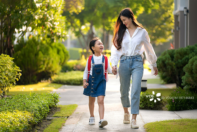 快乐的亚洲母亲和女儿的学前班学生步行上学。课的开始。秋天的第一天。为人父母或爱与联结的表达概念。图片素材