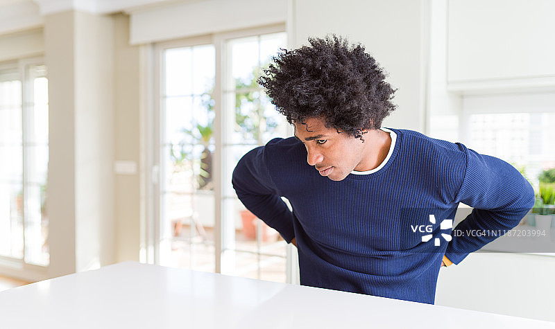 一位年轻的非洲裔美国男子穿着休闲毛衣坐在家里，饱受背痛之苦，用手碰背，肌肉疼痛图片素材