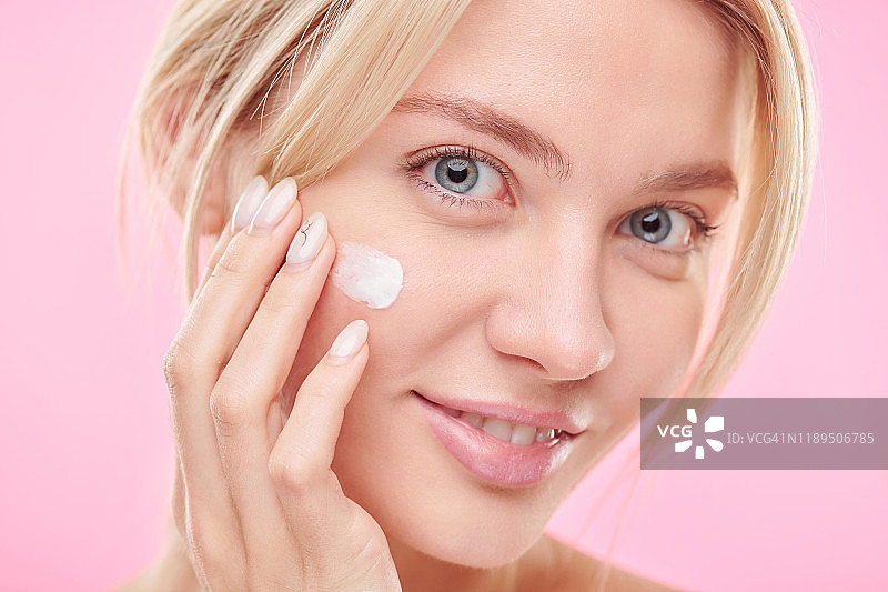 迷人的女性在皮肤护理过程中在脸颊上涂抹保湿霜图片素材