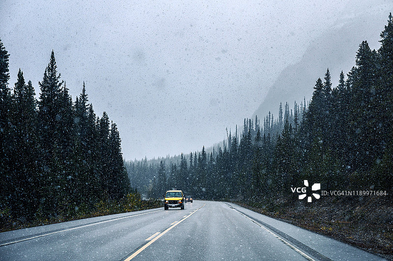 黄色汽车在大雪中行驶在松林公路上图片素材