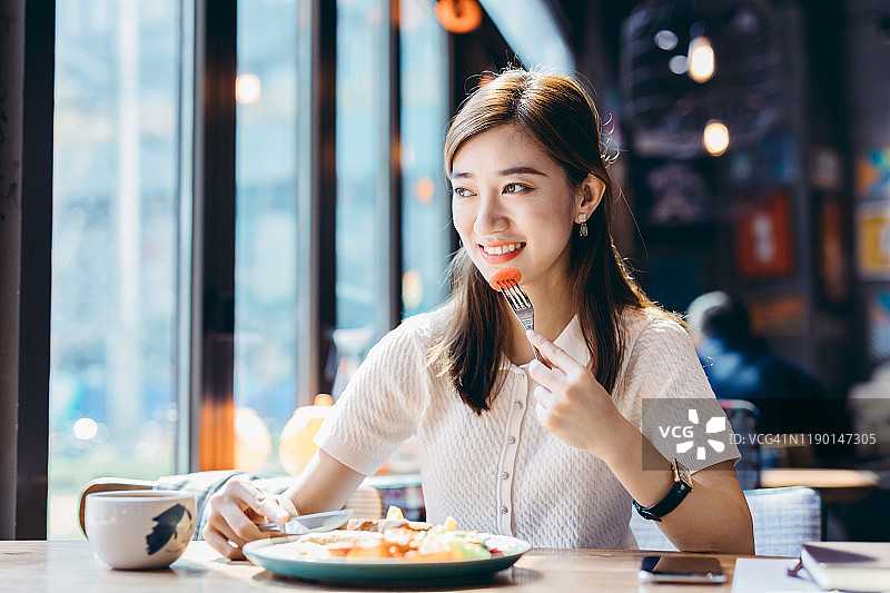 年轻的亚洲女人在咖啡厅吃新鲜的沙拉。图片素材