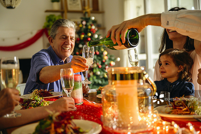 家庭成员在圣诞晚宴上为香槟杯斟酒图片素材