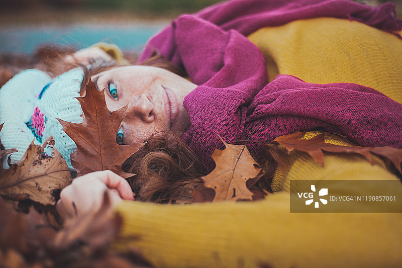 一个年轻的姜黄色女人的肖像躺在一堆秋叶上，穿着时髦的衣服图片素材