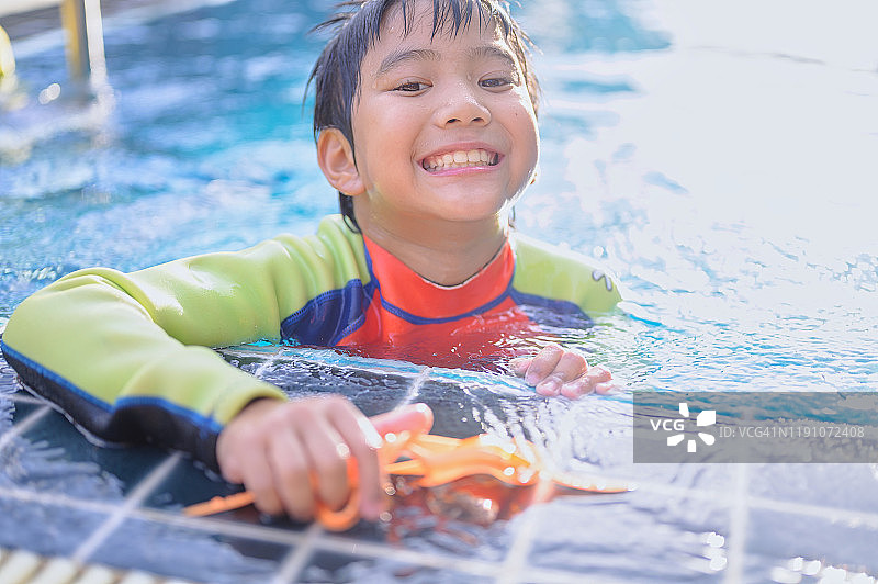 亚洲小孩在一个水上公园游泳池里玩得很开心。被一桶冷水泼后，又笑又叫图片素材