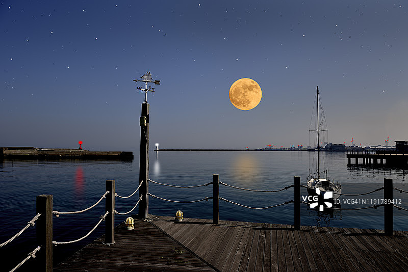 满月升起在帆船风向标和灯塔之上。图片素材