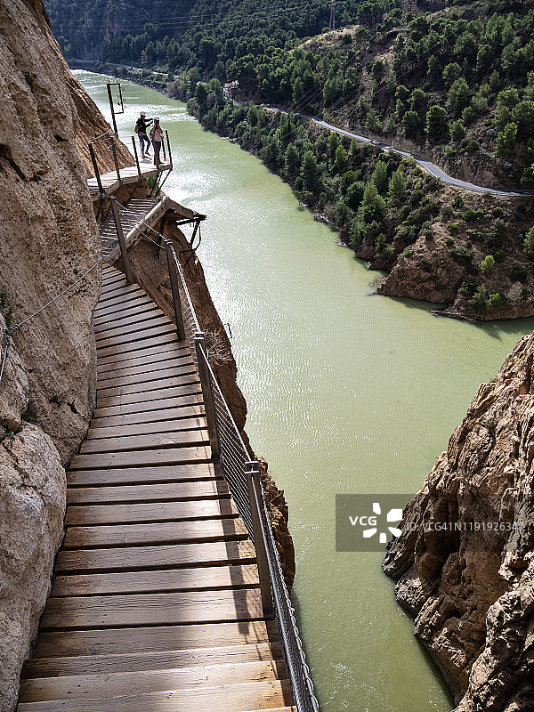 徒步旅行者在大自然中行走在一座木桥上，钉在峡谷的岩壁上达到很高的高度。图片素材