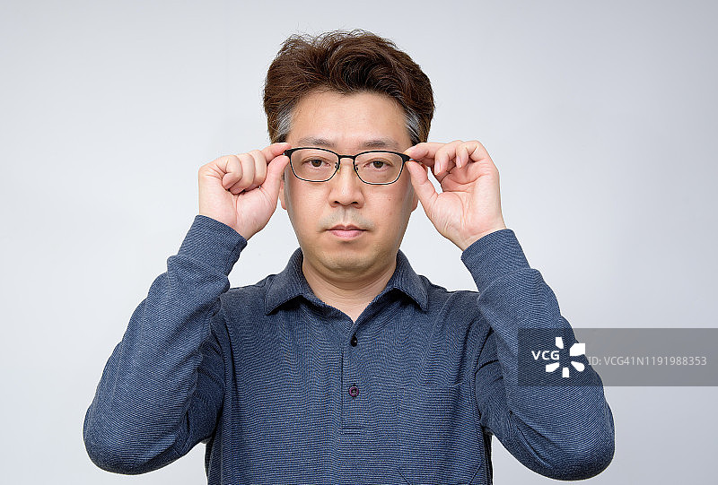 亚洲中年男性试图摘掉眼镜看东西。视力差，老花，近视。图片素材