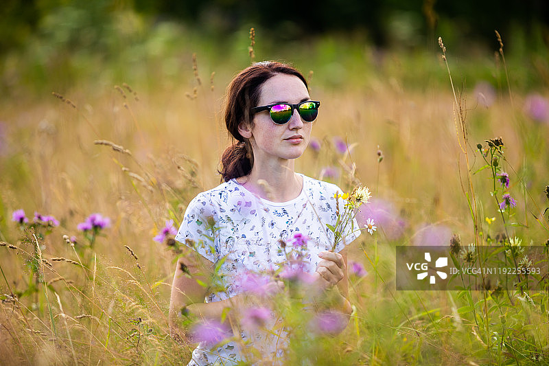 漂亮的年轻女孩戴着太阳镜在一个有花的土地上图片素材