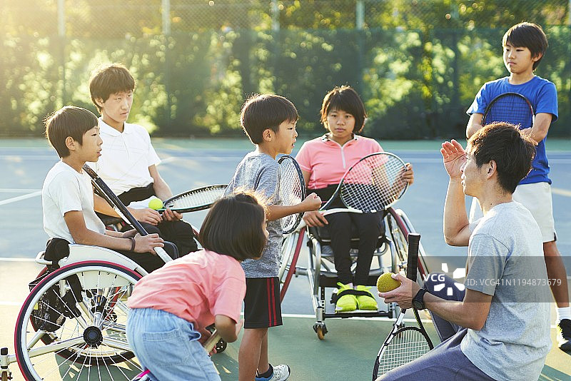 一位网球教练正在和年轻的学生开会，他们有的坐轮椅，有的站着图片素材