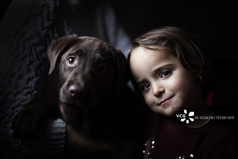 一个女孩和一只棕色拉布拉多小狗的特写，一起摆姿势微笑图片素材