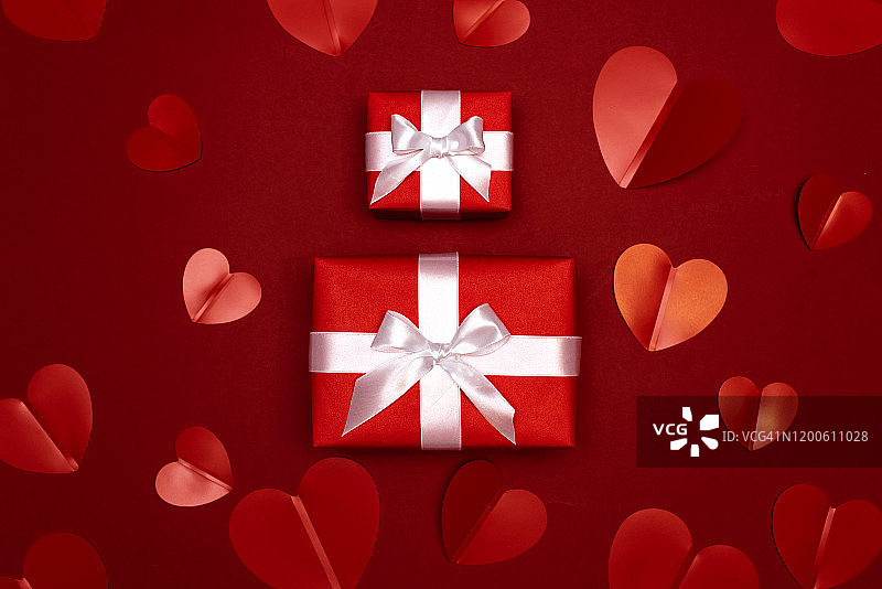 一个礼物在牛皮纸盒与一个红色的蝴蝶结在红色的背景与心。给你的爱人一个惊喜。情人节的概念有婚礼、生日、新年、圣诞节等节日图片素材