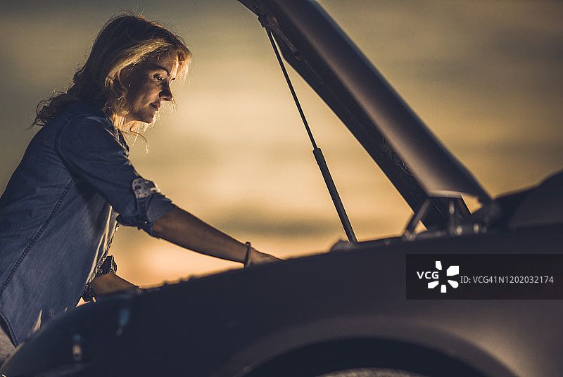 年轻女子在日落时分修理她的破汽车。图片素材