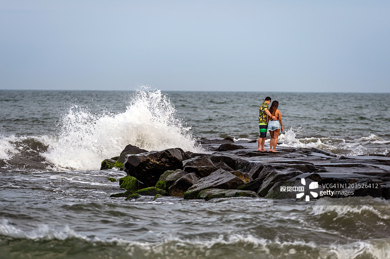 一对浪漫的年轻人在海边的一个石头鼹鼠上。图片素材
