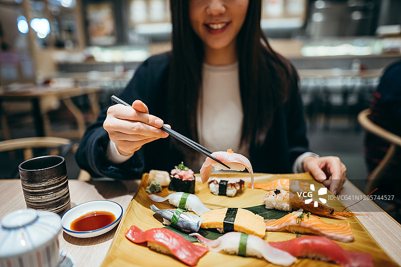 微笑的年轻亚洲女人吃新鲜制作的寿司配菜和绿茶在日本餐厅图片素材