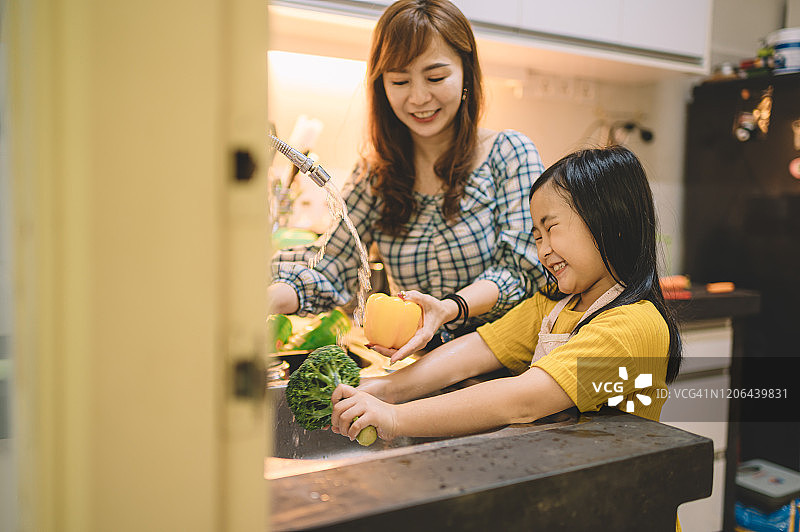 一个亚洲华人母亲在厨房准备食物和她的女儿在粘合时间洗蔬菜花椰菜图片素材