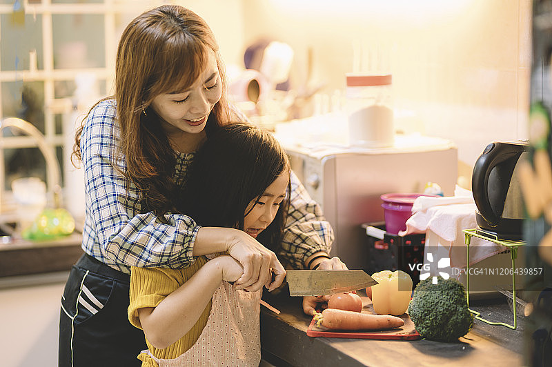 一位亚洲华人母亲在厨房里准备食物，她和女儿在一起切菜图片素材