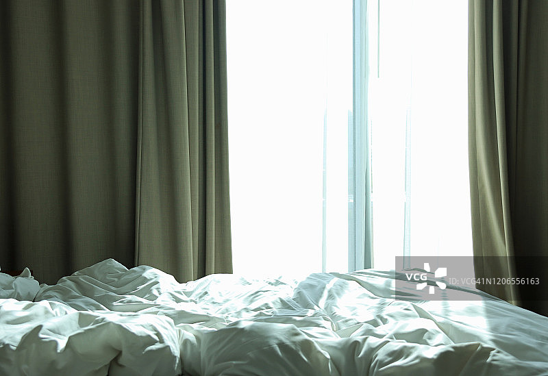 酒店的窗户拉上了窗帘，让明亮的晨光照进来，前景是凌乱的床图片素材