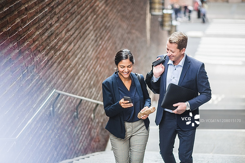 快乐的男性和女性企业家在城市爬楼梯时使用手机图片素材