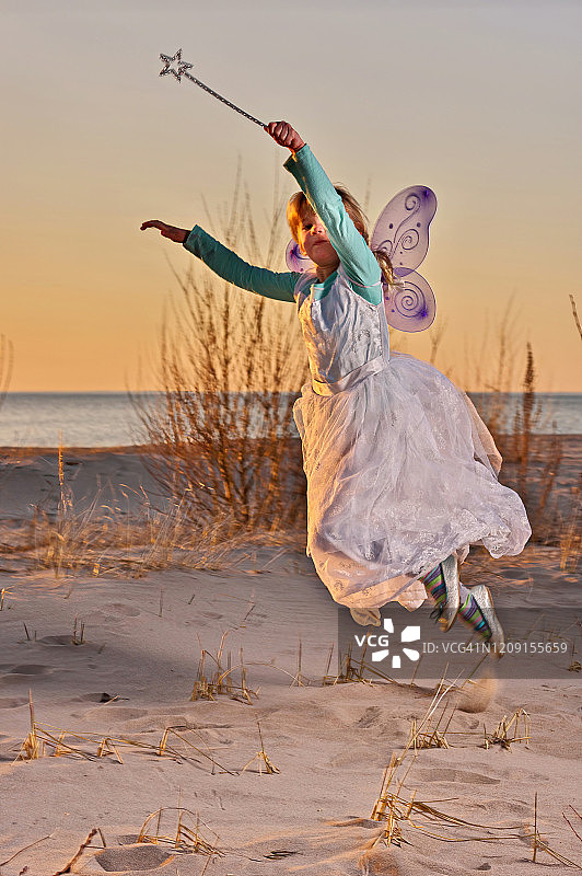 年轻的女孩打扮成一个仙女在日落海滩试图飞翔图片素材