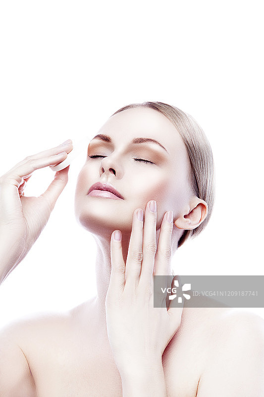 美容模特用手和化妆棉在脸上涂抹护肤霜，保持肌肤健康完美图片素材