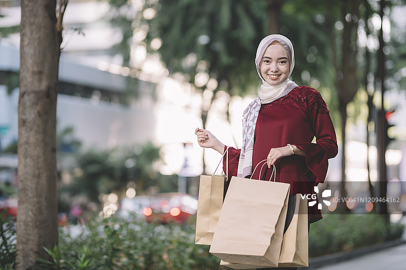 一个亚洲现代马来穆斯林妇女快乐和愉快地走在城市的街道上，她的购物袋图片素材