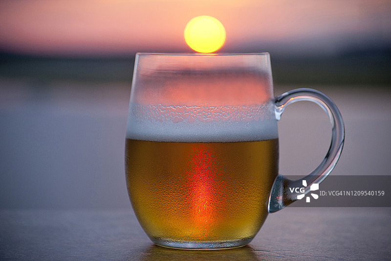 在俯瞰大海的甲板上，一杯啤酒，夕阳刚刚照到边缘图片素材