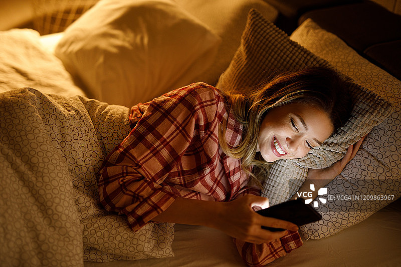 年轻漂亮的女人晚上在床上玩手机图片素材