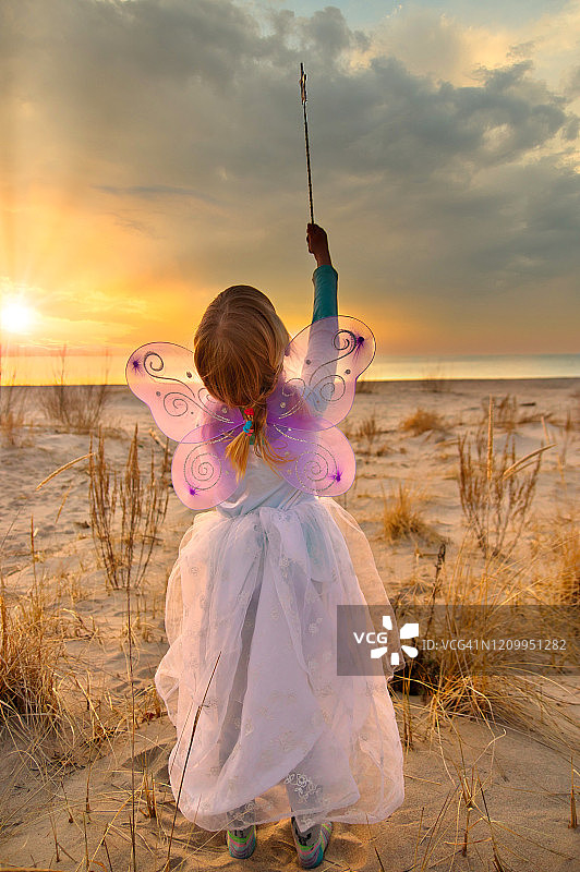 小女孩的偷拍肖像打扮成仙女指向她的魔术棒对天空-后视图图片素材