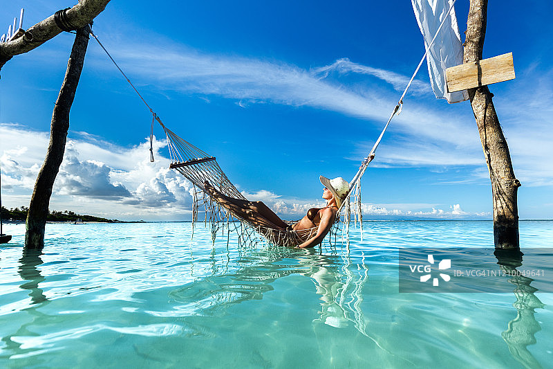 年轻女子在海面上的吊床上晒太阳。图片素材