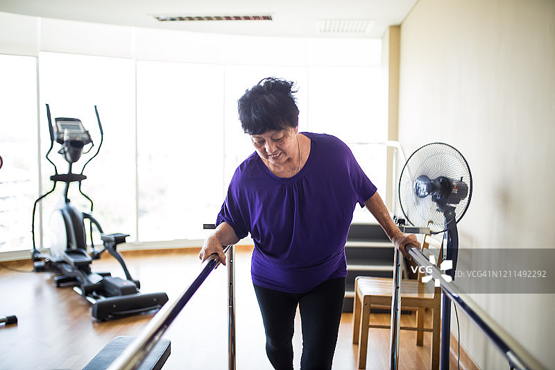 一位老年妇女在康复中心使用双杠行走。图片素材