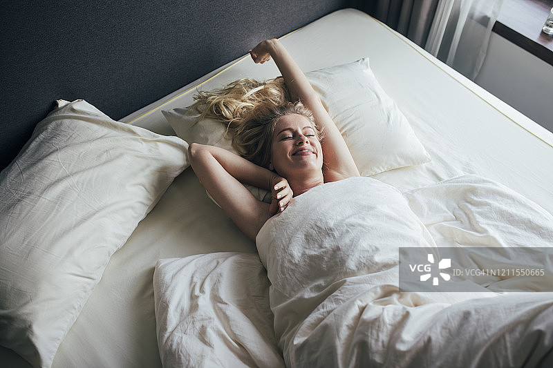 放松的早晨:微笑的长发金发女人醒来后伸展在床上图片素材