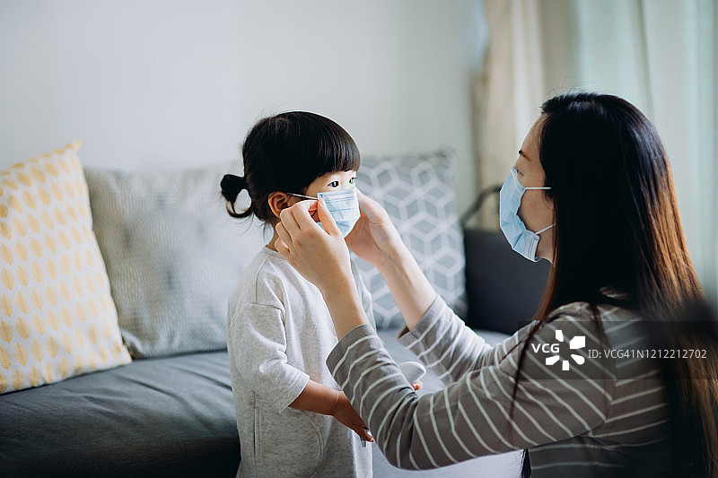 年轻的亚洲母亲在出发前为小女儿戴上外科口罩，以防止感冒、流感和病毒的传播图片素材