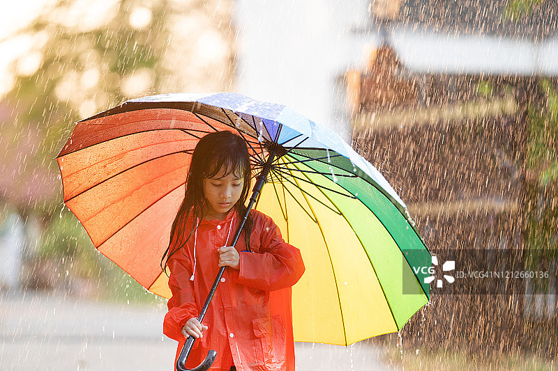 亚洲的孩子们撑着伞在雨中玩耍，她穿着雨衣。图片素材