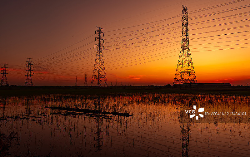 高压塔和电线与日落的天空。电力波兰人。动力和能源概念。工业工厂附近稻田高压电网塔架及电缆。图片素材