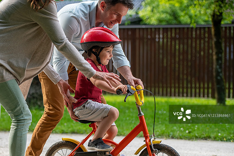 母亲和父亲帮助儿子学习骑自行车图片素材