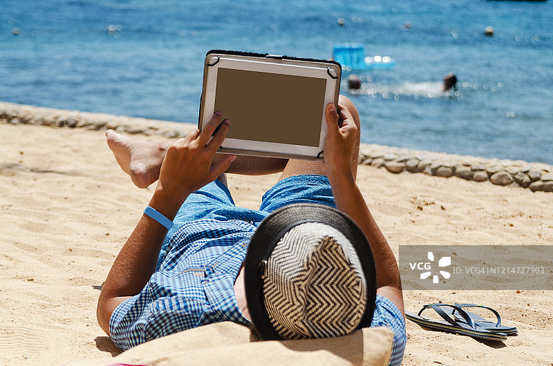 年轻人自由职业者放松做他的工作在海滩上使用平板电脑图片素材