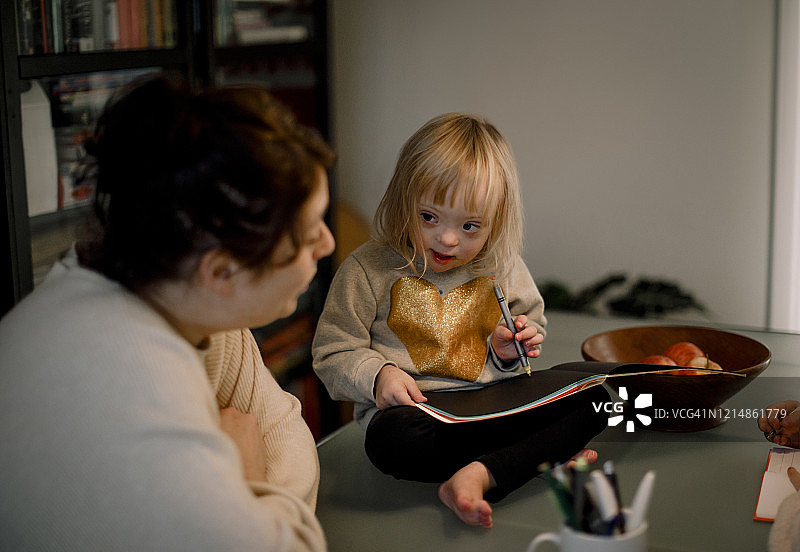 母亲教残疾女儿在家坐在桌子边画画的侧视图图片素材