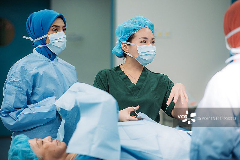 在医院的手术室里，亚裔华裔女护士手拿剪刀，剪手术袍图片素材