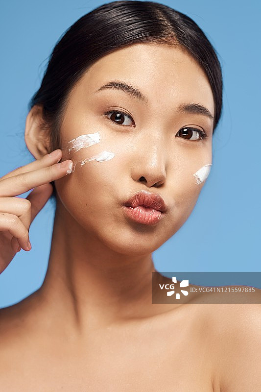 美丽的肖像，一个年轻的亚洲妇女与清洁和健康的皮肤谁应用霜，她的脸。图片素材