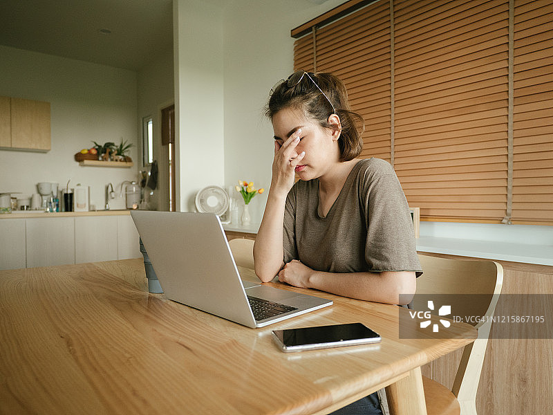 一位亚洲女性在家里使用笔记本电脑时遇到了困难。图片素材