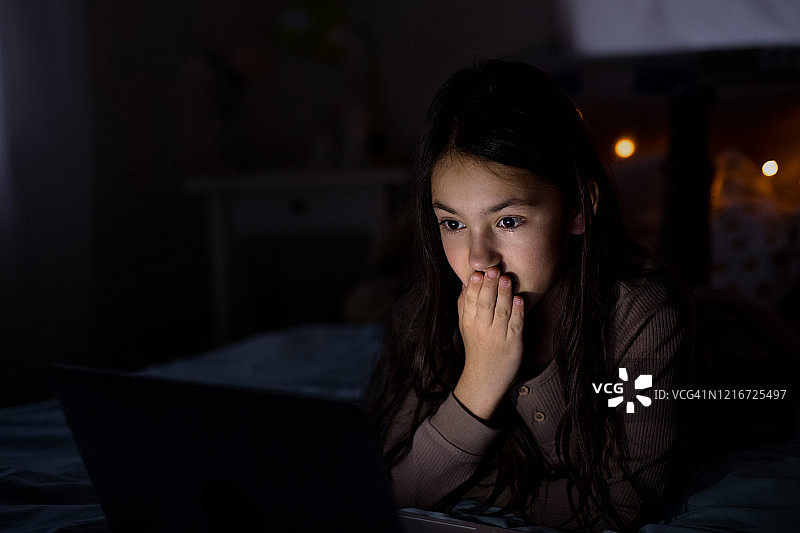 吓坏了的小女孩晚上在电脑前看电影。图片素材