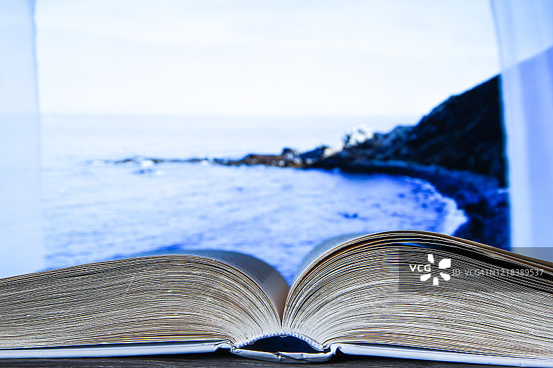 一个精装书的特写在中间打开，打开书，窗口海滩海度假的背景图片素材