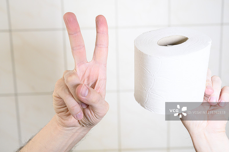 男人在厕所里用另一只手拿着卫生纸做胜利手势。图片素材